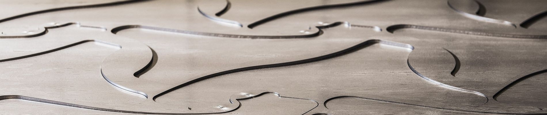 Nahaufnahme von geschichteten Metallplatten mit glatten, geschwungenen Ausschnitten, die fließende, wellenförmige Muster und schattierte Rillen bilden.